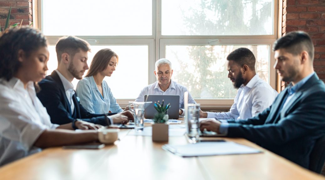 Colleagues Working During Corporate Meeting Sitting At Desk In Office