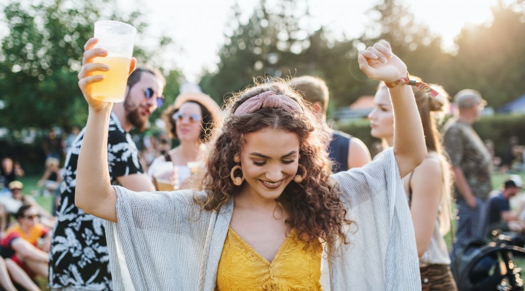 A young woman with drink dancing at summer festival