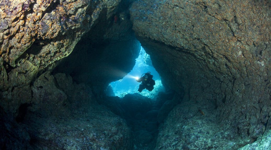 Scuba Diver with LIght Enters Coral Cavern