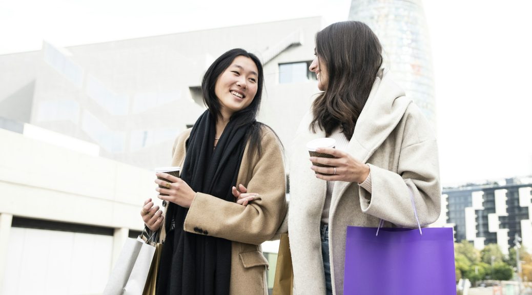 two happy beautiful girls shopping in the city with shopping bags and cup of coffee - fashion and